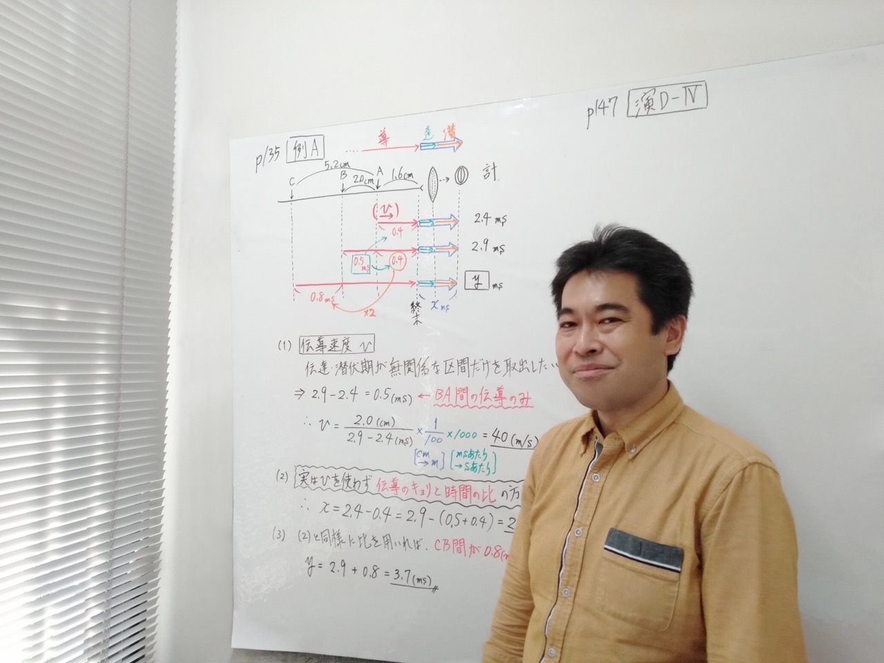 ホワイトボードの板書を背景に微笑む遠藤先生(講師・生物)